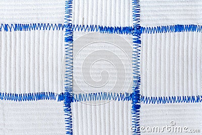 Hand-made textile background of square pieces of white fabrics sewn by blue zigzag seams. Stock Photo