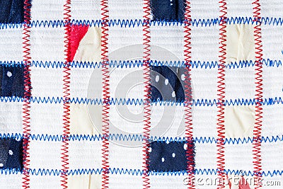 Textile pattern of square pieces of colored fabrics, sewn by red and blue zigzag seams on white fabric. Stock Photo