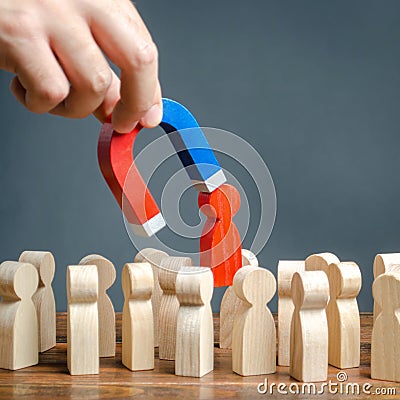 The hand with a magnet pulls out a red figure of a man from the crowd. Increase team efficiency, productivity. leader manages Stock Photo
