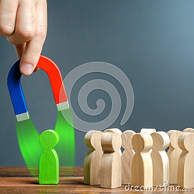 A hand with a magnet is trying to pull a green figure near the crowd of people. Recruiting new workers. Formation Stock Photo