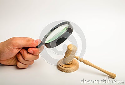 The hand with the magnifying glass gazes intently at the hammer of the judge. The concept of investigation of court cases. Corrupt Stock Photo