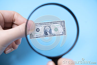 Hand with a magnifying glass looks at a small dollar on a blue background Stock Photo