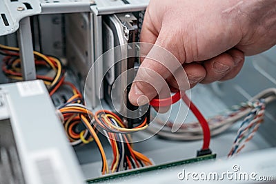 Hand of man plugging SATA Serial AT Attachment, Serial ATA data cable in hard drive device. Computer bus interface to connect ma Stock Photo