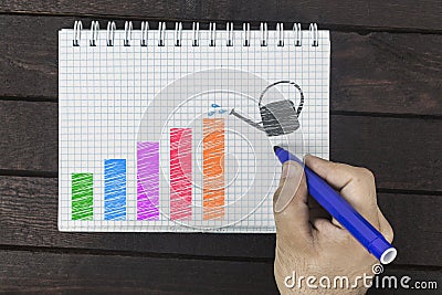 Hand with a marker drawing colored diagram chart with watering can showing growth on notepad Stock Photo