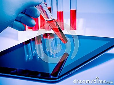 Hand in medical blue glove hold a test tube near modern digital tablet in laboratory Stock Photo