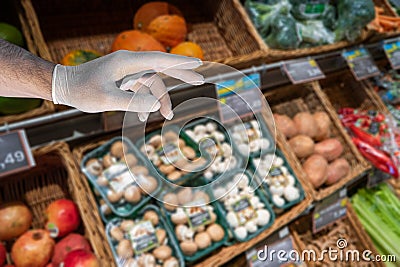 A hand in medical glove is trying to take food over grocery shelve shop with fresh vegetables and fruits, details, closeup Stock Photo