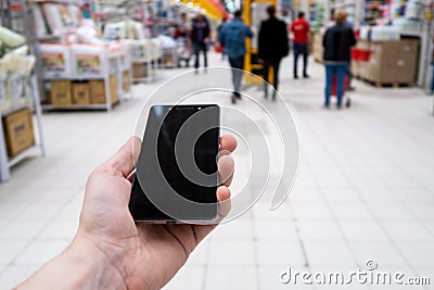 Hand with mobile phone on a background of a blurry shopping center. Stock Photo