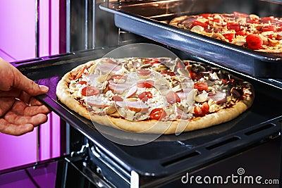 Hand moves the tray of pizza with mushrooms, ham and mozzarella Stock Photo