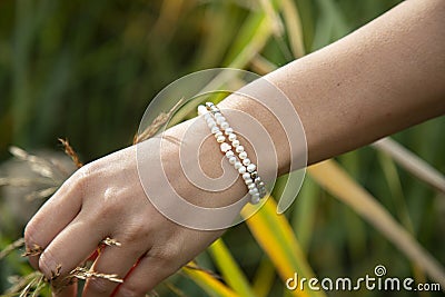 Hand outdoor touching plants with pearl and hematite bracelet Stock Photo