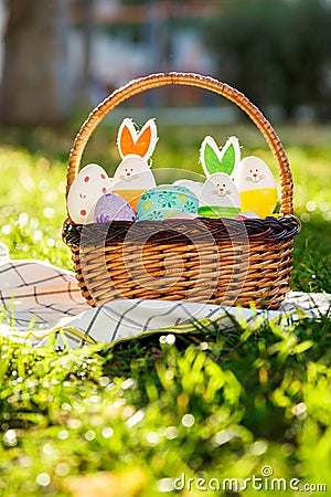 Hand painted Easter eggs and bunny in big rattan basket on green grass on white towel. Traditional decoration for Easter Stock Photo