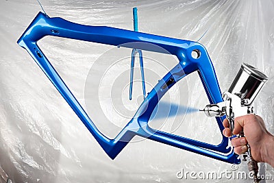 Hand of painter with spray gun producing a shiny new fresh paintwork coating paint of a metallic blue carbon racing road bicycle Stock Photo