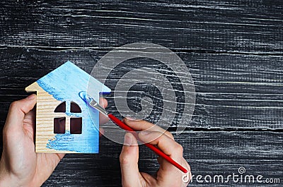 Hand paints a house in to blue color. Concept of repair, hobby, work. Repair and painting of wooden house figurines. Toy house Stock Photo