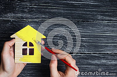 Hand paints a house in to yellow color. Concept of repair, hobby, work. Repair and painting of wooden house figurines. Toy house Stock Photo