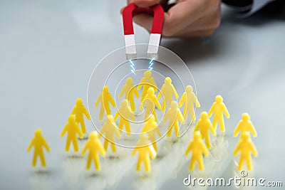 Hand Of A Person Attracting Group Of Figurines With Magnet Stock Photo