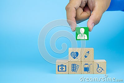 Hand picking up doctor icon on cube wooden toy blocks with medical icons stacked. Stock Photo