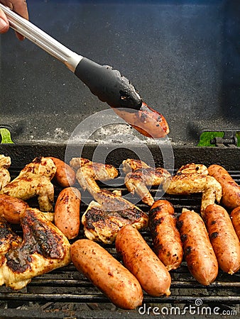 Hand with pincer placing a sausage on the grill Stock Photo