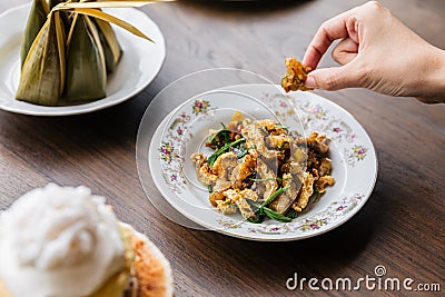 Hand pinching Stir Fried Spicy Crispy Pork Skin with Acaci. Classic Thai cuisine Stock Photo