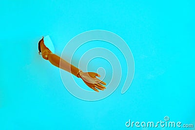 hand of a plastic doll break through torn blue paper creative minimalistic still life Stock Photo