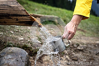 Hand is pouring spring water into mug at mountains Stock Photo