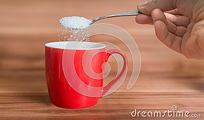 Hand is pouring sugar to red cup of tea. Unhealthy eating concept Stock Photo