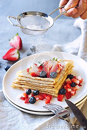 Man`s hand powdering icing sugar on crepes, summer breakfast Stock Photo