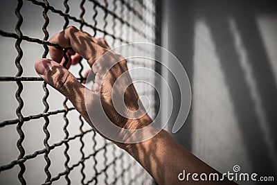 Hand of prisoner holding rustic metal fence with pattern shadow, criminal locked in jail Stock Photo