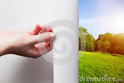 Hand pulling edge of a paper to uncover green landscape Stock Photo