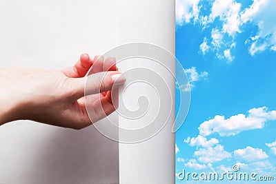 Hand pulling edge of a paper to uncover, reveal blue sky Stock Photo