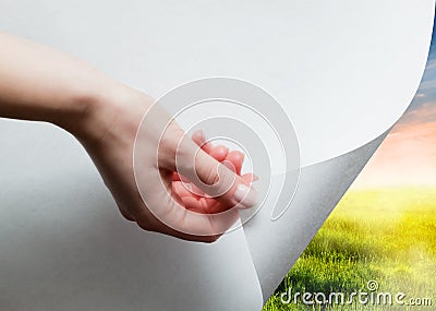 Hand pulling a paper corner to uncover, reveal green landscape Stock Photo