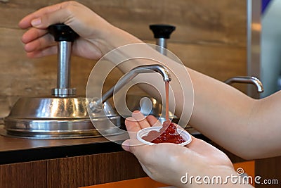 Hand pumping ketchup from sauce pump in to small plastic bowl in fast food restaurant Stock Photo