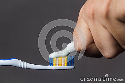 hand puts toothpaste on the toothbrush on a gray background close-up Stock Photo