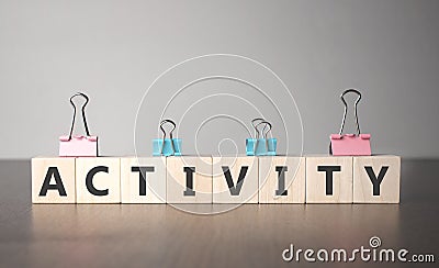 The hand puts a wooden cube with sign activity. The word is written on wooden cubes standing on the dark table on the grey Stock Photo