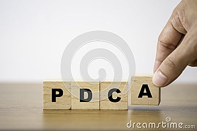Hand putting P D C and A which print screen on wooden cube block. Plan Do Check and Action is continuous quality improvement Stock Photo