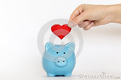 Hand putting red heart into piggy-bank. Stock Photo