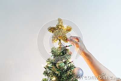 Hand putting sparkling golden star on Christmas tree for decorating and celebration in Christmas Holiday Stock Photo