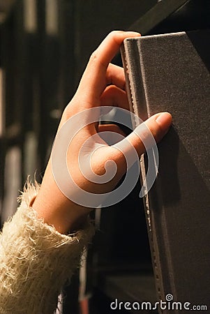 Hand reaching for book on a shelf Stock Photo