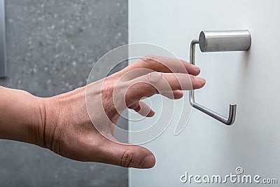 A hand reaching for an empty toilet paper holder Stock Photo