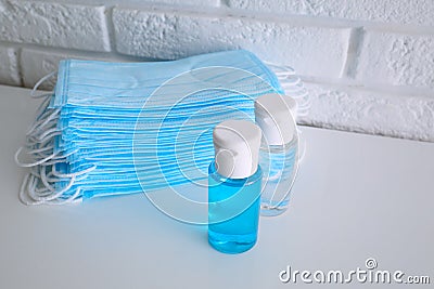 Hand sanitizers and respiratory masks on table near white brick wall. Protective essentials during COVID-19 pandemic Stock Photo