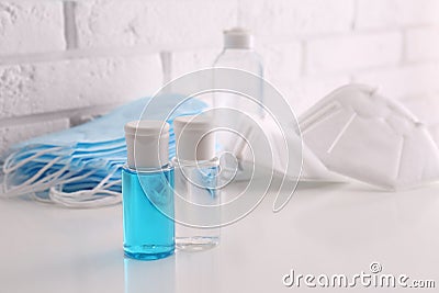 Hand sanitizers and respiratory masks on table near white brick wall. Stock Photo