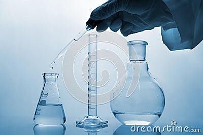 Hand of scientist dropping water in glass science flask with cylinder in blue medical science laboratory Stock Photo