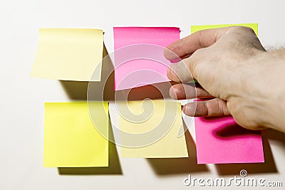 A hand shoots multi-Colored square post-it notes pasted on a white wall Stock Photo