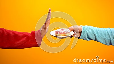 Hand showing stop sign rejecting glazed donut on bright background, weightloss Stock Photo