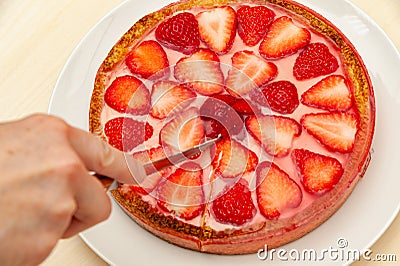 Hand slicing the best homemade strawberry tart. Isolated on wooden background. Stock Photo