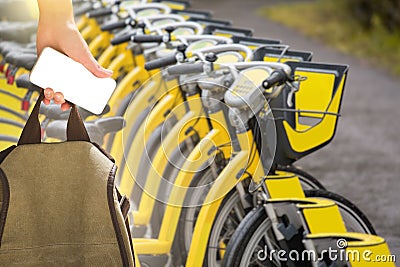Hand with a smartphone and a backpack in front of a row of rental bikes. Stock Photo