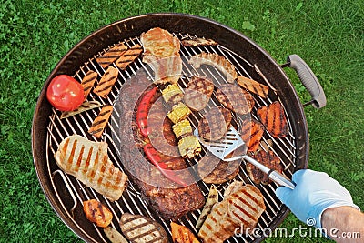 Hand With Spatula And BBQ Grill With Meat And Vegetables Stock Photo