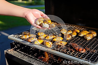 hand spreading butter over smoking clams on a grill Stock Photo