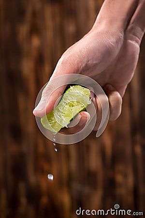 Hand squeeze lime with lime drop on dark wooden background Stock Photo