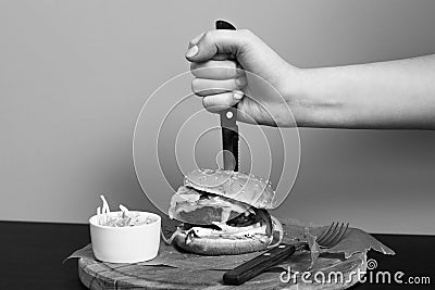 Hand stubbing burger with knife Stock Photo