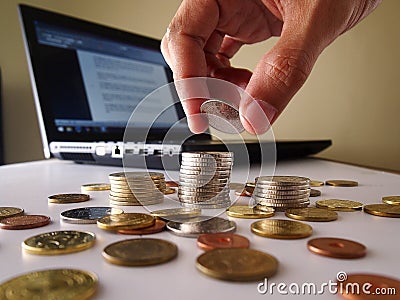 Hand Stacking up coins and a laptop computer Stock Photo