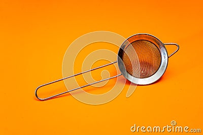Hand strainer with fine metal mesh insulated on orange bottom. Kitchen utensils Stock Photo